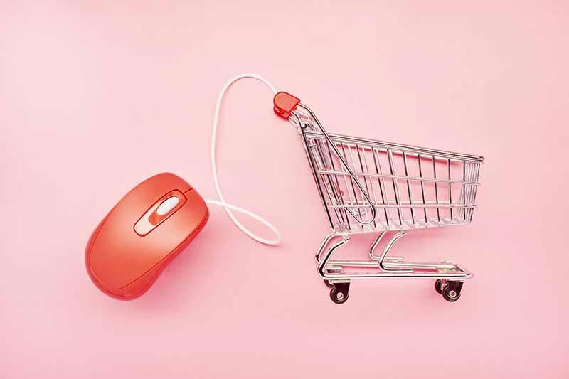 still life of a small shopping cart and red computer mouse on pink background, online shopping