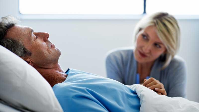 wife sitting by husband in hospital bed