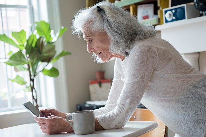 Woman looking at her cell phone while leaning on kitchen counter